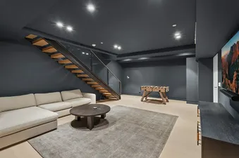 A modern basement games room in Maison Cornet featuring a beige sectional, a foosball table, and a wall-mounted TV.