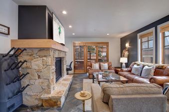 A spacious living room at Town Pointe A105 featuring a large stone fireplace, comfortable sofas, and a television above the mantel, perfect for relaxing after a day outdoors.