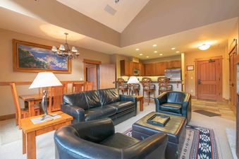 A spacious living room with leather sofas and armchairs, a wooden coffee table, and a large painting on the wall.