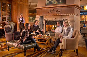 A group of people are enjoying drinks and conversation in a cozy lounge area with a fireplace.