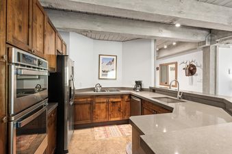 A modern kitchen in Enclave 211 with wooden cabinets, stainless steel appliances, gray countertops, and a ski poster on the wall.