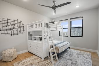 A modern children's bedroom at Mayflower Lakeside 204 featuring white bunk beds with an integrated dresser, a ceiling fan, and large windows with exterior views.