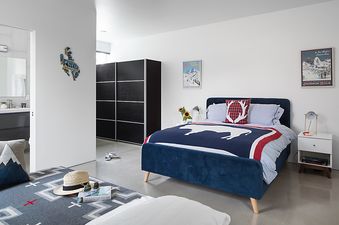 A modern minimalist bedroom featuring a blue velvet bed frame and an en-suite bathroom at Taminah Retreat.