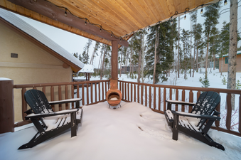 A cozy winter patio with two snow-covered Adirondack chairs and a chiminea, offering a rustic outdoor retreat.
