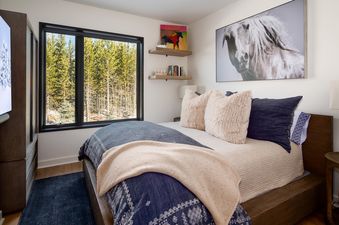 The bedroom in Moonlight Basin 215 Lakelodge features a king bed, a large window with a view of the trees, and a cozy, comfortable atmosphere.