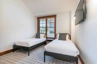 A bedroom with two twin beds, a television, and a window with a view of the forest.