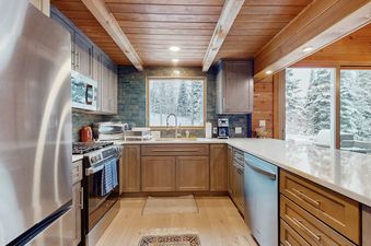 Modern kitchen with wood cabinets, stainless steel appliances, and a snow-filled forest view from the window at the Wood Road House.