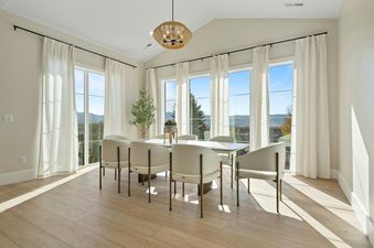 A modern dining room in the TimpView Bundle with a white table, chairs, and large windows offering scenic mountain views.