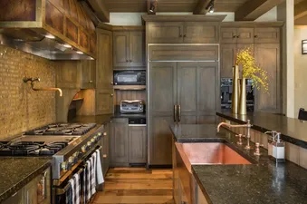 A sophisticated gourmet kitchen with dark wood cabinetry, black granite countertops, stainless steel appliances, and a prominent copper sink.