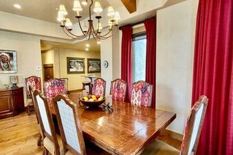 A large dining room with a long wooden table and eight chairs, illuminated by a large chandelier.
