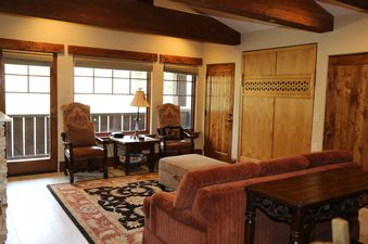 A cozy, rustic living area with plush seating, wooden accents, and a large rug, bathed in natural light.