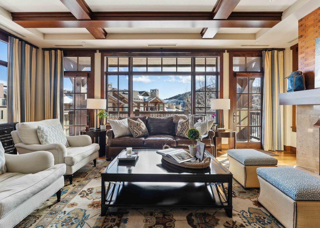 Spacious living room with leather sofa, two armchairs, and coffee table, showcasing a view of the mountain landscape through large windows.