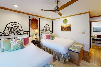 A bedroom with two twin beds, a ceiling fan, and a dresser with a lamp.