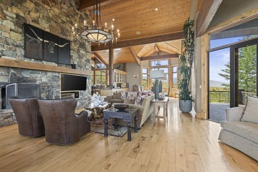 A large living room with a stone fireplace and floor-to-ceiling windows offering a view of the mountains.