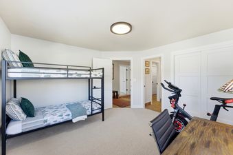 The light and airy bedroom featuring a metal bunk bed with green and white bedding, an exercise bike, and multiple doorways leading to other rooms.