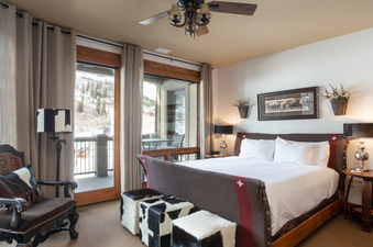 The master bedroom in 132 Two Bedroom Black Diamond Lodge features a king-sized bed with a plush white duvet and a large window with views of the mountains.