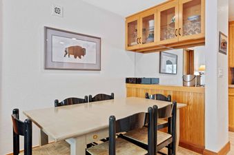 A cozy dining area at The Charter D4105 with a light wooden table, six chairs with woven seats, and built-in wooden cabinetry above a mirrored backsplash.