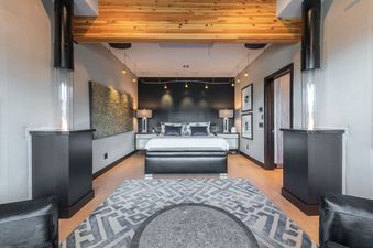 A modern bedroom with a large bed, two black end tables with lamps, a long modern rug, and two black fireplaces.