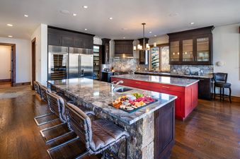 A modern kitchen with dark wood cabinets, stainless steel appliances, a marble island, and hardwood floors. A charcuterie board is displayed on the island.