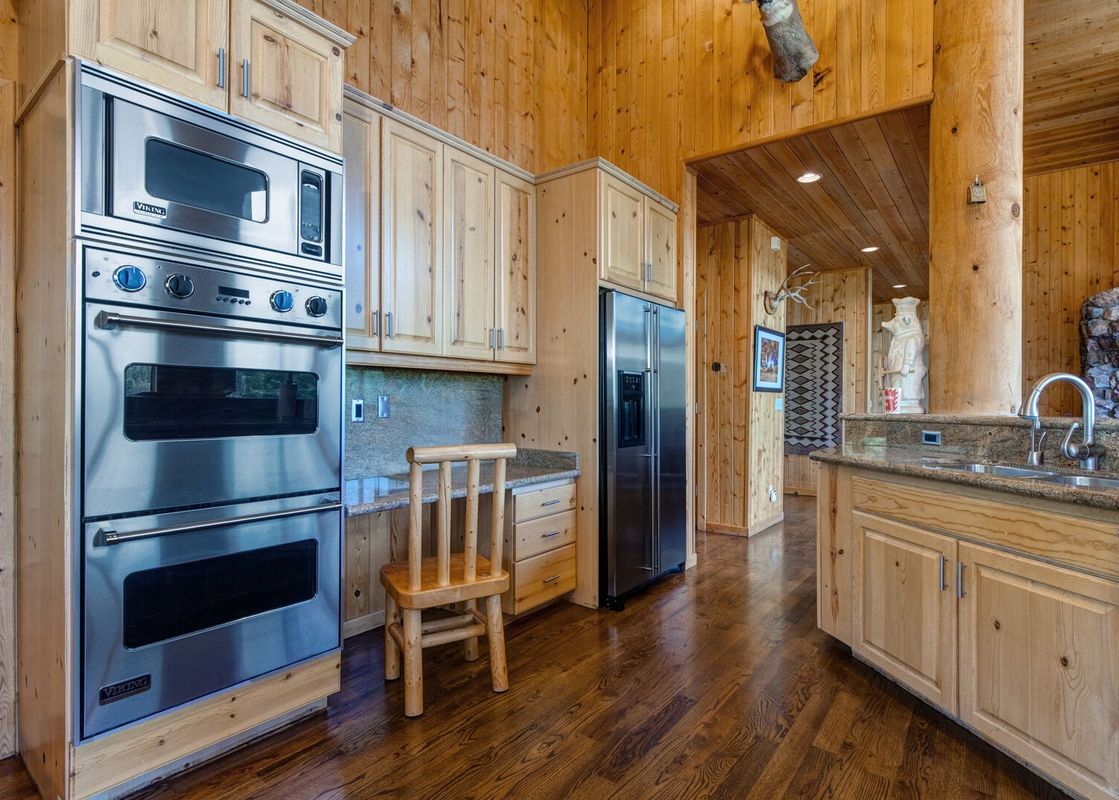 A spacious kitchen with rustic wood finishes, stainless steel appliances, and a granite countertop island with a sink.
