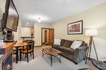 A cozy living room in Pines Unit 120 with a brown sofa, coffee table, dining area, and a fireplace.
