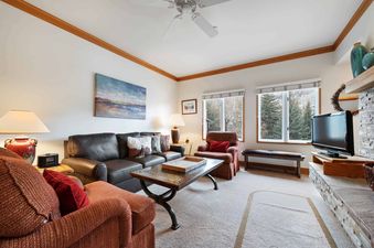 A cozy living room in The Charter D2205 featuring a dark leather sofa, two red armchairs, a wooden coffee table, a flat-screen TV, and large windows with natural views.