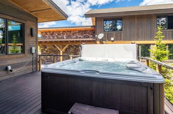 The hot tub at Moonlight Basin 8 Alpine Bend is positioned on a deck with a wooden railing and a view of the surrounding mountains.