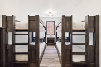 A cozy bunk room at Moonlight Ridge featuring two dark wooden bunk beds, white bedding, and a central window overlooking a rustic wooden wall.