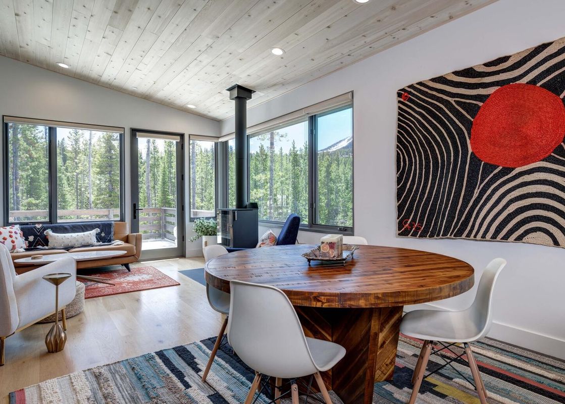 The open floor plan of Moonlight Basin 12 Lake Cabin includes a large dining room table with chairs, a living room area with a couch and coffee table, and a wood-burning fireplace.