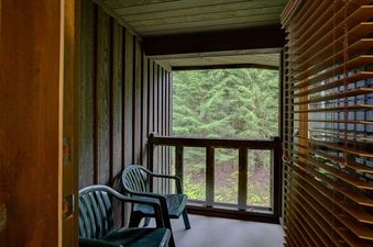 A cozy, private balcony with two green chairs offers a serene forest view.