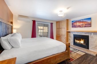 A cozy bedroom in Resort Plaza 5024 featuring a wooden bed, a fireplace, and a window with red curtains.