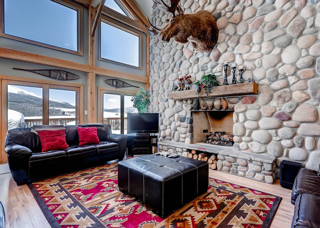 The Snow Mountain Lodge living room features a stone fireplace and views of the mountains.