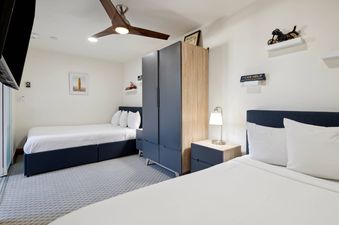 A modern secondary bedroom at The Charter L222 with two beds, a closet, nightstand, ceiling fan, and decorative accents.