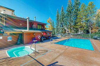 The outdoor pool and hot tub at the Phoenix are sparkling under a clear blue sky, surrounded by vibrant green trees.