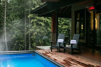 A private outdoor pool with blue water and two lounge chairs with white towels on a wooden deck, surrounded by a lush forest.