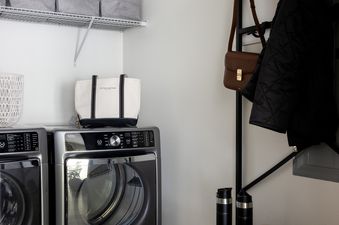 A modern and organized laundry room featuring a washer and dryer, shelves with storage bins, and a stylish black and wood storage unit with accessories.