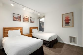 A bright bedroom at Snow Flower 129 Park City with two twin beds, desert-themed artwork, and track lighting, featuring a window and an air vent.