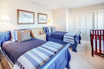 A serene bedroom with two blue twin beds, each with blue and plaid bedding, a wooden nightstand, and framed artwork on the light-colored walls.