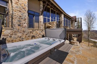 An inviting hot tub with bubbling water on a flagstone patio, set against a stone-faced building under a clear blue sky, offers a perfect spot for relaxation at Snow Pine Lodge at Deer Valley.