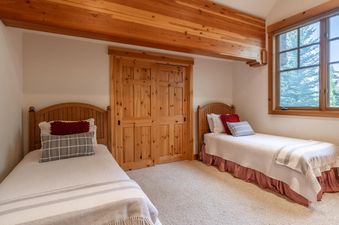 A cozy twin bedroom at Northstar Sierra Gold Home, featuring two wooden-framed beds with white bedding, decorative pillows, and a large window overlooking green trees.