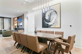 An elegant dining area in Founders Place 2503 featuring an oval marble table with tan leather chairs under a modern glass chandelier.