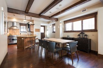 A wide-angle view captures the spacious open-concept kitchen and dining area of Silver Star 404, featuring dark wood flooring, a modern stainless steel kitchen, a rustic dining table with gray chairs, and large windows.
