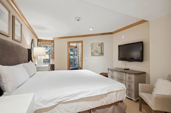 A hotel room with a king sized bed, a TV, and a dresser.