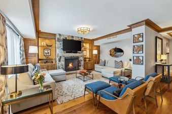 A luxurious and spacious living room in the St Regis Executive Suite features comfortable seating, a stone fireplace, and elegant wooden accents.