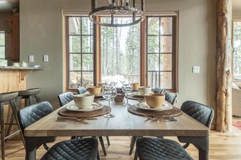 A dining table set for a meal in a room with large windows overlooking a snowy forest.