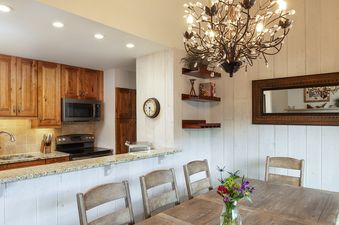 A bright open-concept kitchen and dining area at Vantage Point 504 featuring wooden cabinetry, granite countertops, and a dining table with a decorative chandelier above.