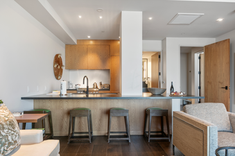 A modern kitchen with a breakfast bar, stools and a couch in the living room.