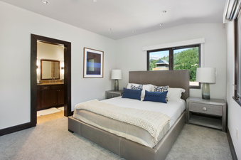 The bedroom in Lumiere Three Bedroom Penthouse features a plush king-sized bed, a large window with mountain views, and a bedside table with a lamp.