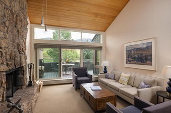 The living area features a stone fireplace, comfortable seating, and a large sliding glass door leading to a balcony with an outdoor dining area.