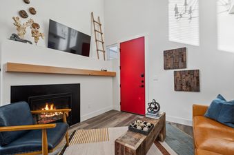 A modern living room with a lit fireplace, a wall-mounted TV, and a vibrant red entry door.